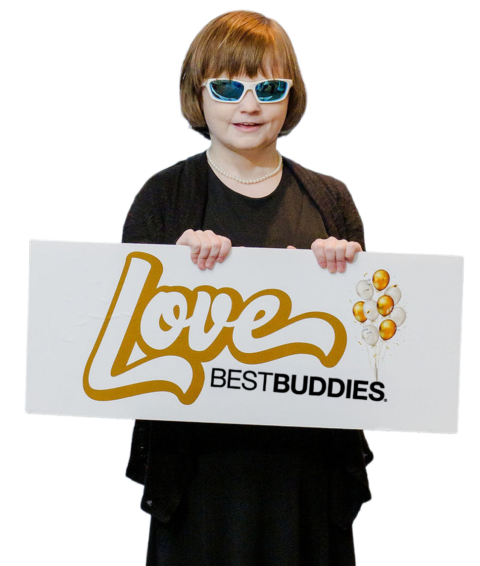 The image shows a young girl standing and holding a rectangular sign in front of her. She’s wearing a black outfit, a short necklace, and white-framed sunglasses with blue-tinted lenses. Her hair is a short, neat bob with bangs. She’s smiling slightly while holding a sign that reads “Love BEST BUDDIES” in stylized lettering—“Love” is written in a large gold script, and “BEST BUDDIES” appears below it in black. There’s also a small cluster of gold and white balloons printed on the right side of the sign. The background is plain/transparent, which makes the subject and the sign stand out clearly.