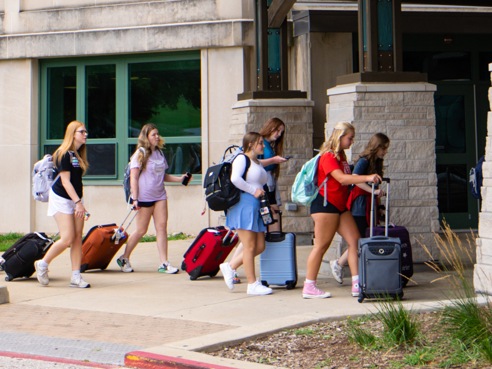 Group of student leaders rolling suitcases towards a dorm.