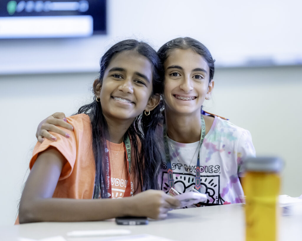 Two young girls sitting next to each other at a table smiling