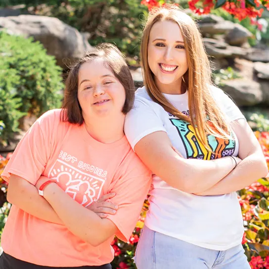 Two female Best Buddies participants smiling while standing back to back