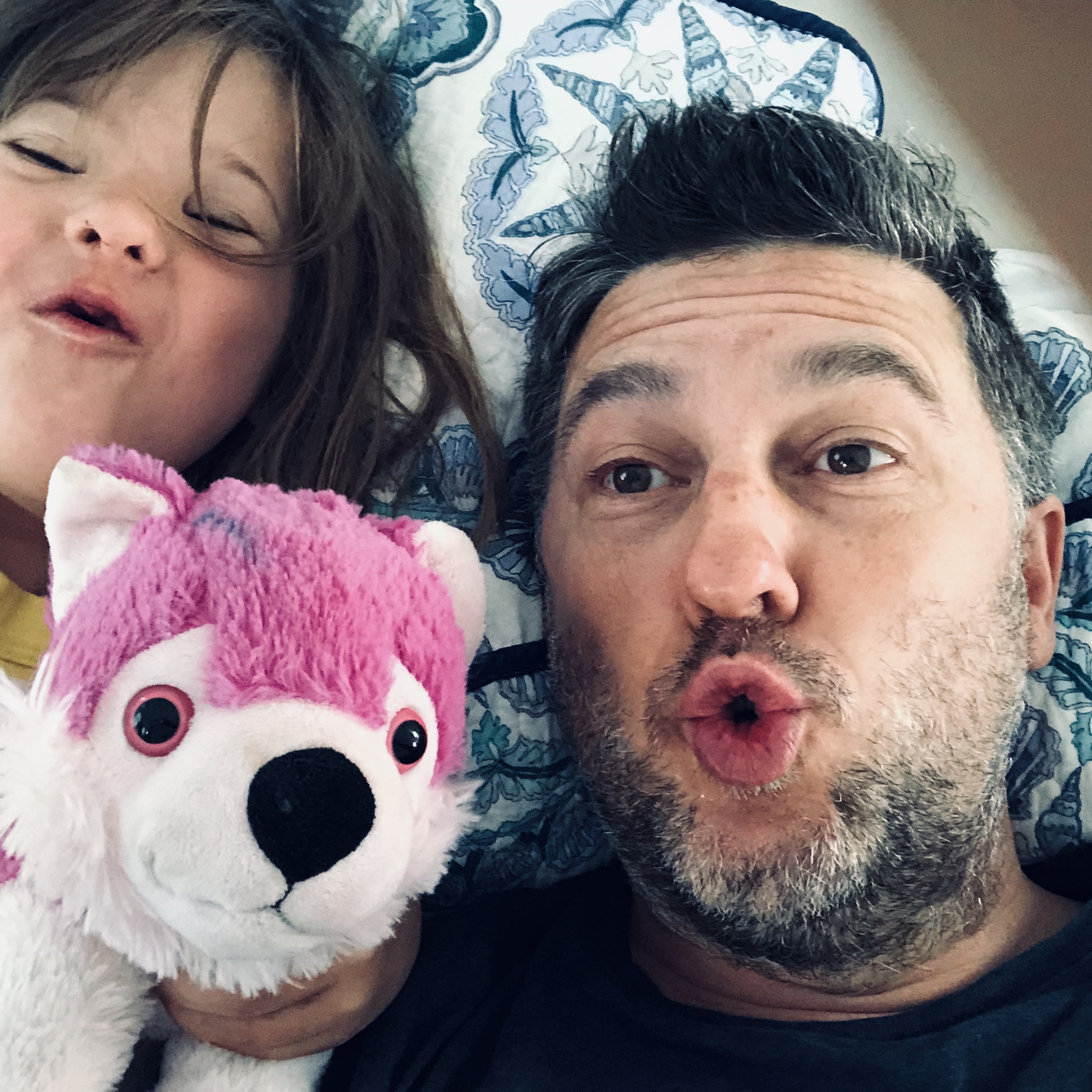 young girl with older man laying down with a white and pink stuffed animal