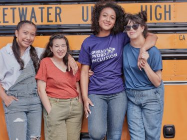 four female students standing in front of a school bus