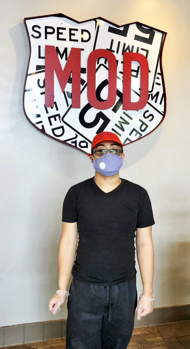 Chris, a Best Buddies Jobs Participant and Mod Pizza Employee, stands in Front of the Mod Pizza indoor sign