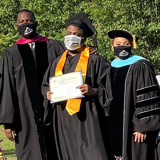 Three Graduates from Appalachian State University in their graduating attire. The middle graduate is holding his diploma.