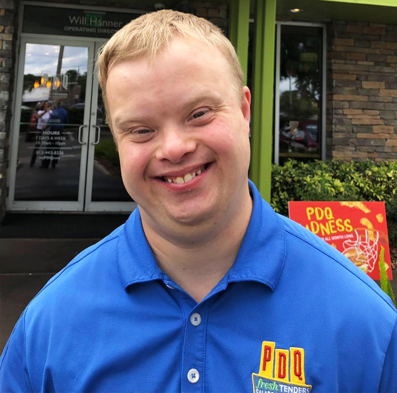 Sam Piazza, an advocate for people with disabilities, has been working at a Tampa PDQ for eight years. He is pictured smiing and proudly wearing his PDQ green uniform and black baseball styled hat.