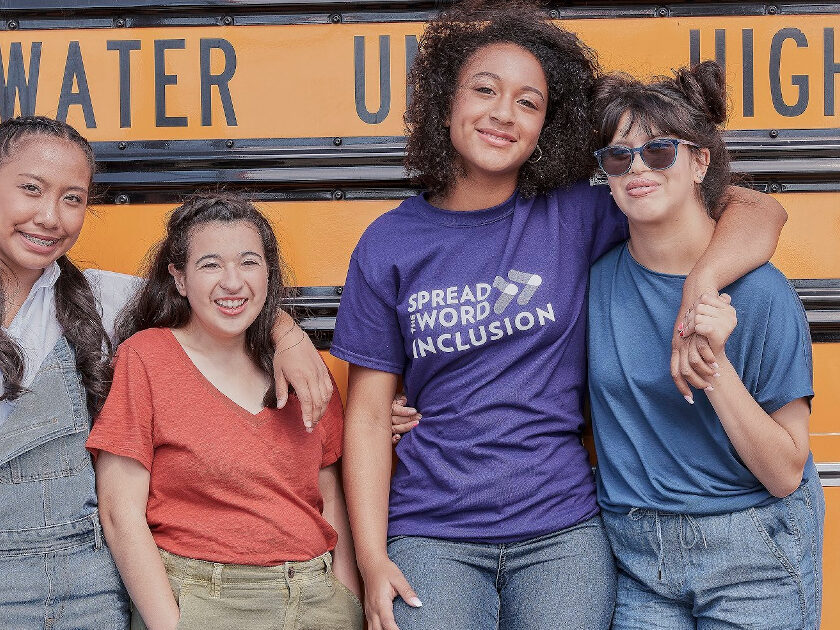 Four teenage females standing in front of a school bus smiling