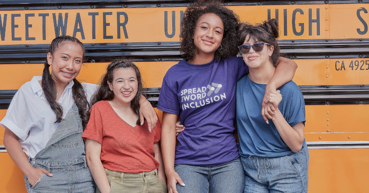 Four teenage females standing in front of a school bus smiling