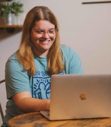 Young woman sitting at table, smiling while looking at a laptop