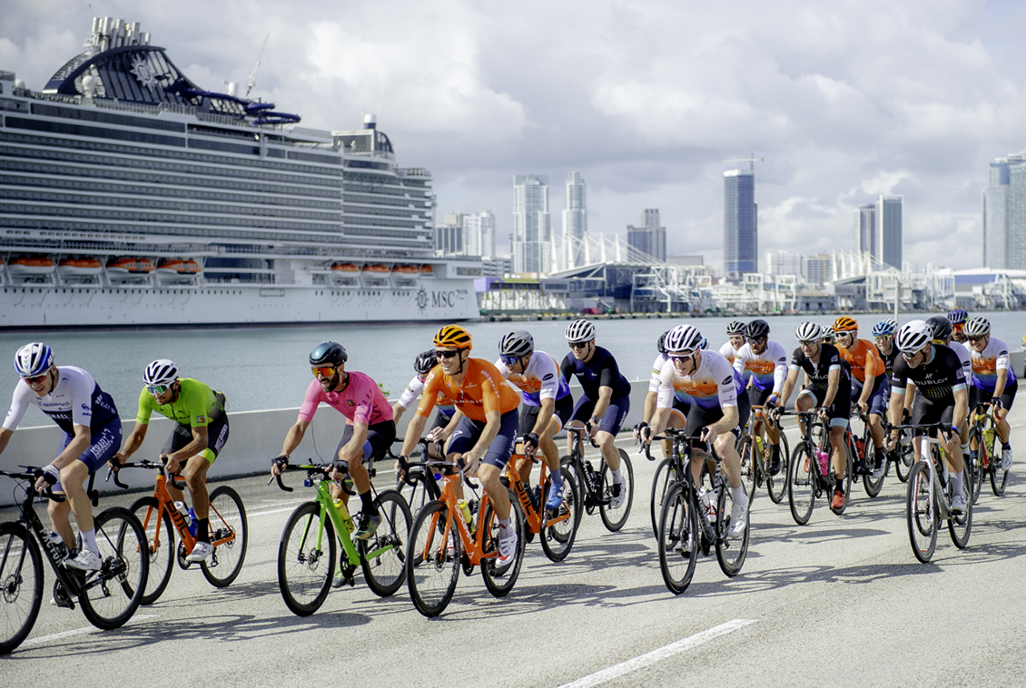 A group of cyclists ride in the Best Buddies Challenge: Miami over the the MacArthur Causeway. The downtown Miami skyline and the cruise ship in the Port of Miami can be seen in the background.
