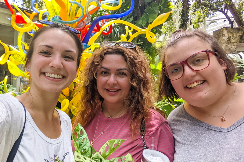 3 female Best Buddies Miami Living Program Participants, pose in front of a Dale Chihuly glass sculpture.