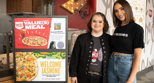 Best Buddies Supporter, Olivia Cumpo, and a female Best Buddies participant are shown inside a MOD's Pizza, next to a Mod's Pizza Value Meal sign.