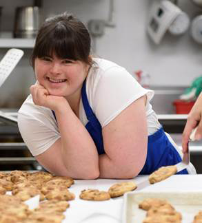 Collette Divitto, owner of Collettey’s Cookies is smiling in front of a batch of cookies.