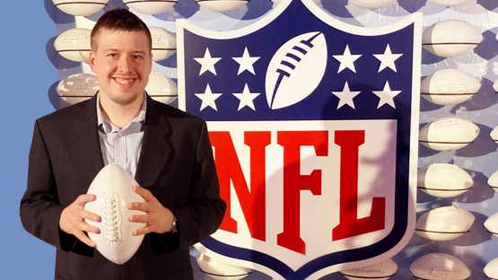 Jobs Participant, Zack Smith is holding a white football next to an NFL sign.