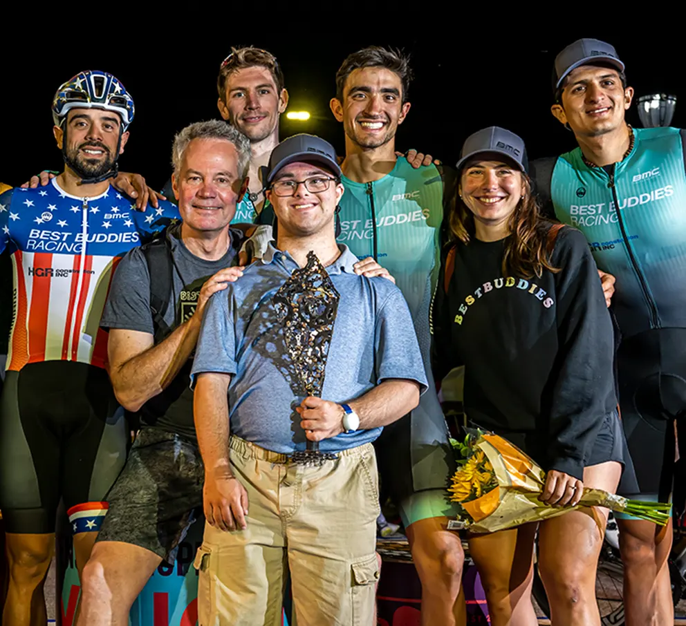 Best Buddies Racing Team surround a Best Buddies participant holding a trophy at one the the cycling events.