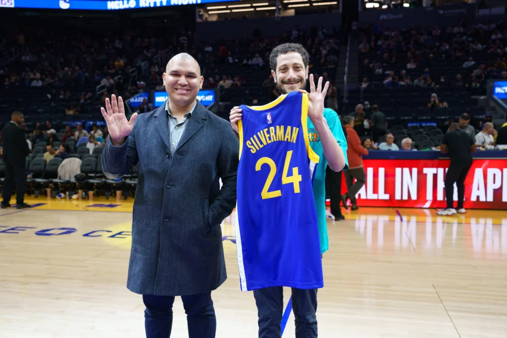 Aaron Silverman waving to the camera with a commemorative Warriors jersey