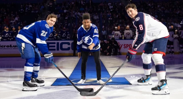 Joshua Felder, Best Buddies Ambassador, stands alongside two hockey players on the ice rink, captivating a large crowd.