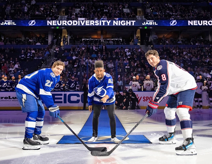 Joshua Felder, Best Buddies Ambassador, stands alongside two hockey players on the ice rink, captivating a large crowd.