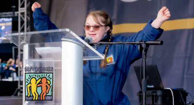 Best Buddies participant celebrates on stage while speaking at a podium during the Best Buddies Challenge: Hyannis Port event.