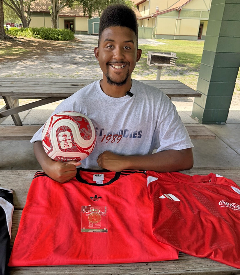 Best Buddies ambassador Joshua Felder displays FIFA Club World Cup memorabilia, including a soccer ball, jerseys, and credential, after representing Best Buddies at the international tournament.