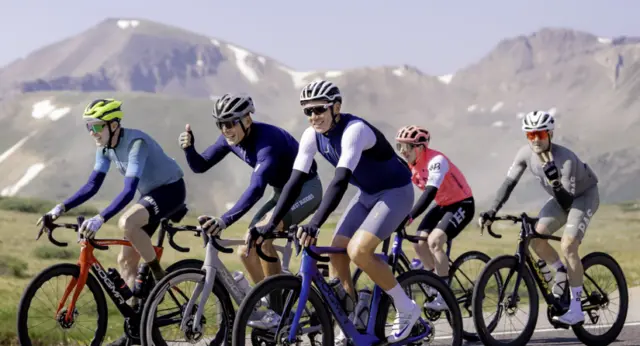 A group of cyclists rides together through a scenic mountain landscape during the Best Buddies Challenge: Aspen, celebrating endurance, teamwork, and inclusion.