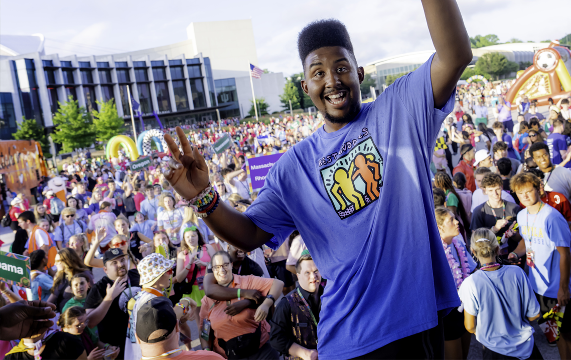 A Best Buddies participant smiles and waves to a large crowd gathered outside during the Best Buddies Leadership Conference, celebrating an energetic and inclusive event.