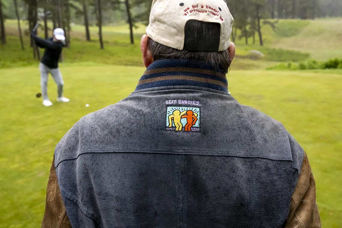 2026 News Golf 7 Golfer wearing a Best Buddies jacket watches another golfer tee off on a rainy golf course