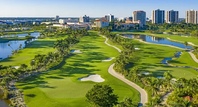 2026 News Golf featured image Aerial view of a coastal golf course with water, palm trees, and city buildings.