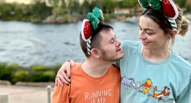 2026 Siblings Post Two smiling siblings wearing festive holiday Mickey Mouse ears share a warm moment by the waterfront, with one arm around the other's shoulders.
