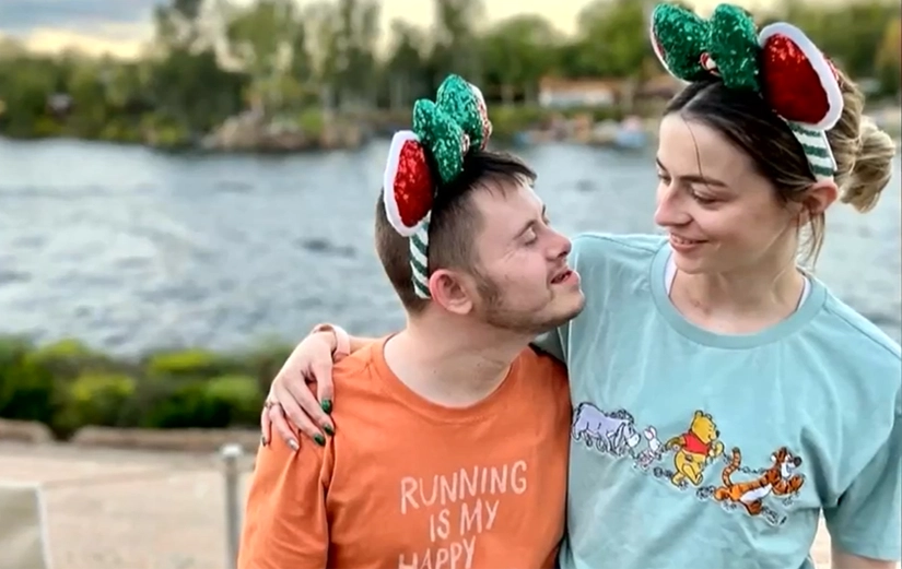 2026 Siblings Post Two smiling siblings wearing festive holiday Mickey Mouse ears share a warm moment by the waterfront, with one arm around the other's shoulders.