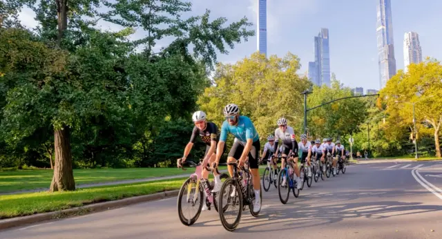 2026 abc7ny post Alt tag image Group of cyclists riding through Central Park in New York City, with lush green trees and Manhattan skyscrapers in the background.