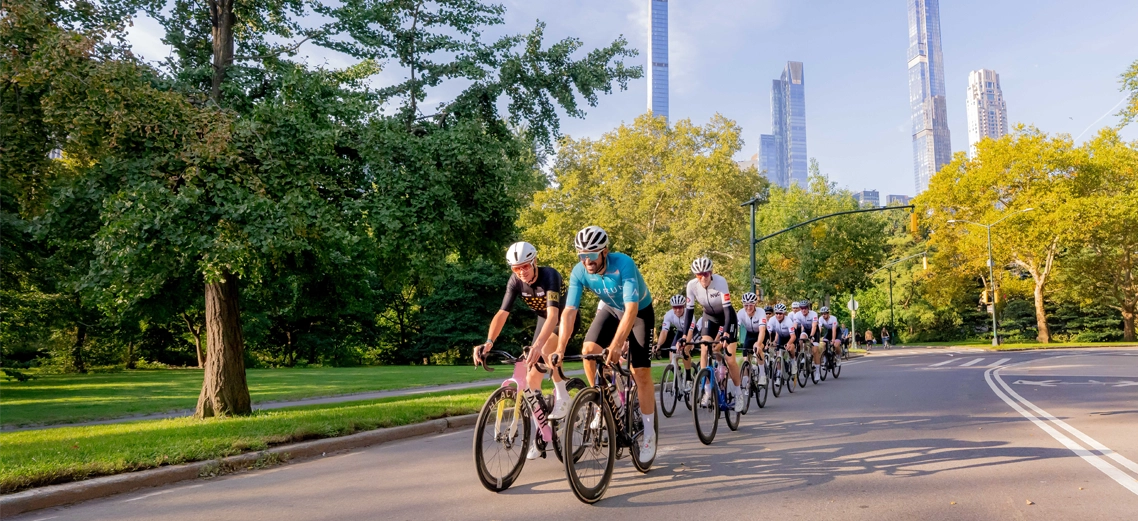 2026 abc7ny post Alt tag image Group of cyclists riding through Central Park in New York City, with lush green trees and Manhattan skyscrapers in the background.