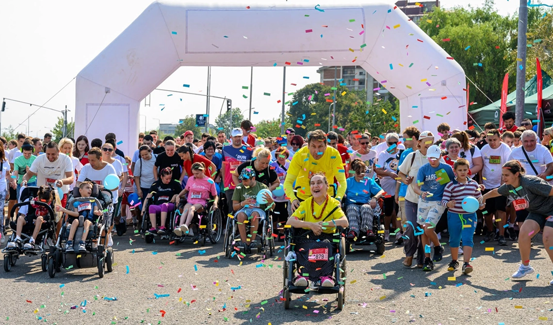News - North Macedonia Launch Post image 1 Best Buddies participants and supporters cross the starting line of an outdoor Friendship Walk as colorful confetti fills the air.